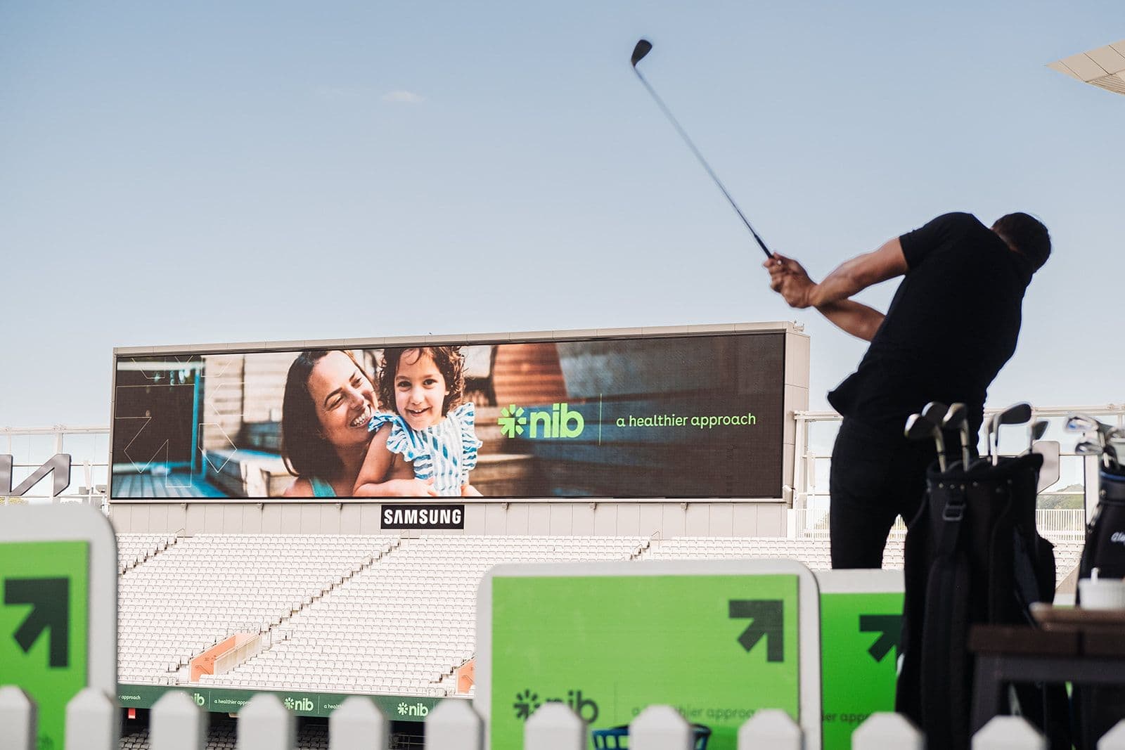 Person swinging golf club at eden park towards an Nib billboard.